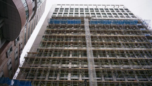 Close-up of a building facade covered in scaffolding and protective mesh during construction or renovation. London, England - Starpik Stock