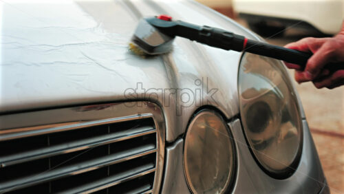 Close up of a car hood being scrubbed with a brush and water - Starpik Stock