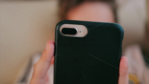 Close up of a child holding a smartphone with a black case while lying down indoors - Starpik Stock