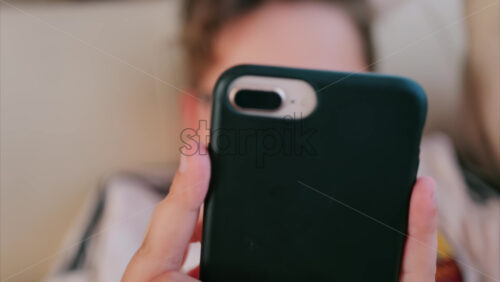 Close up of a child holding a smartphone with a black case while lying down indoors - Starpik Stock