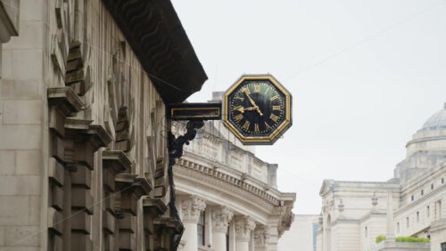 Close-up of a decorative black and gold clock mounted on a historic stone building in London, England - Starpik Stock