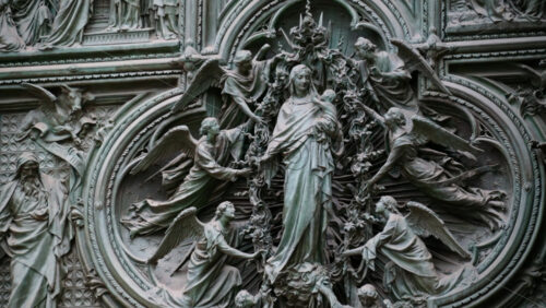 Close up of a detailed relief sculpture of the Virgin Mary holding the infant Jesus, surrounded by multiple angels on the Duomo in Milan, Italy - Starpik Stock