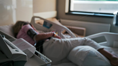Close-up of a fetal monitor in a doctor’s office, displaying fetal heart rate and uterine contraction data during a prenatal check-up with a blurred view of a pregnant woman lying in a hospital bed - Starpik Stock