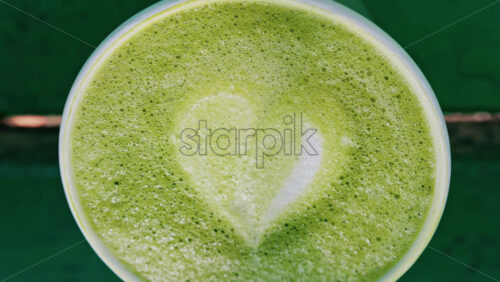 Close up of a frothy matcha latte with heart-shaped latte art - Starpik Stock