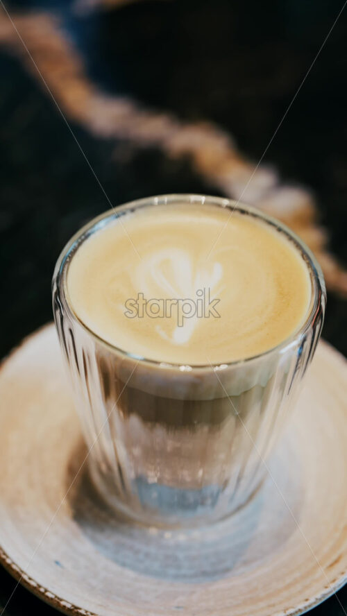 Close up of a glass cup with a latte at a cafe. Vertical - Starpik Stock