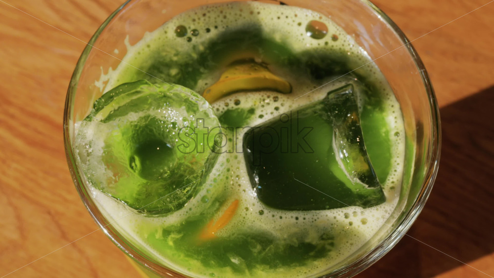 Close up of a glass of an iced orange juice matcha on a table at a cafe - Starpik Stock