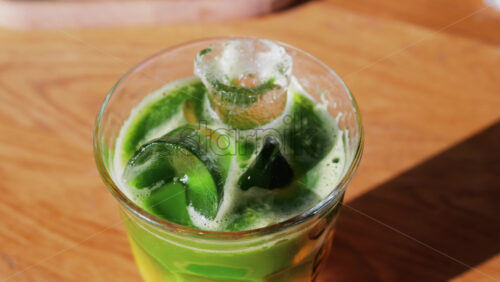 Close up of a glass of an iced orange juice matcha on a table at a cafe - Starpik Stock
