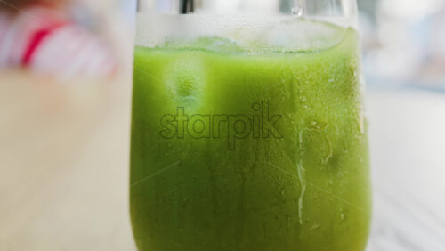 Close up of a glass of an iced orange juice matcha on a table at a cafe - Starpik Stock