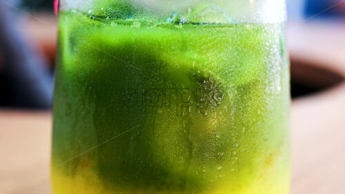 Close up of a glass of an iced orange juice matcha on a table at a cafe - Starpik Stock