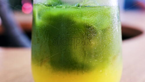 Close up of a glass of an iced orange juice matcha on a table at a cafe - Starpik Stock
