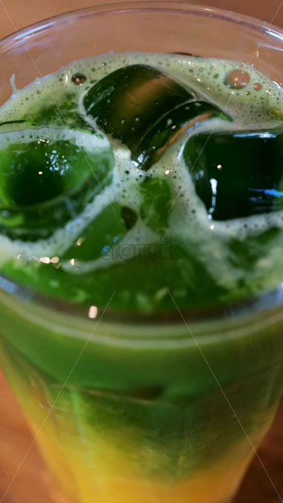 Close up of a glass of an iced orange juice matcha on a table at a cafe. Vertical - Starpik Stock