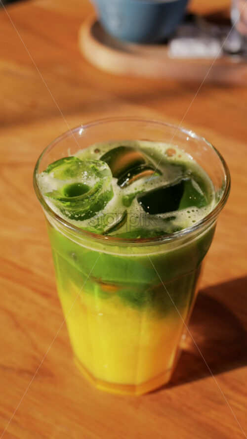 Close up of a glass of an iced orange juice matcha on a table at a cafe. Vertical - Starpik Stock