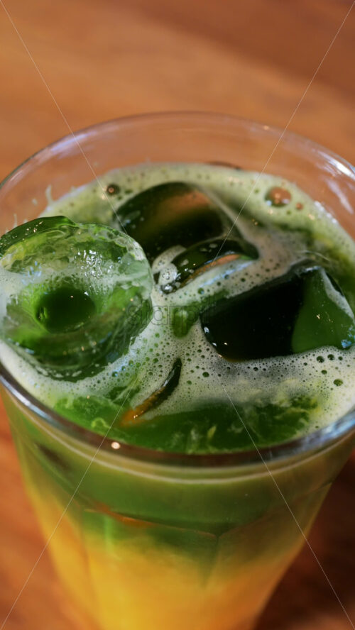 Close up of a glass of an iced orange juice matcha on a table at a cafe. Vertical - Starpik Stock