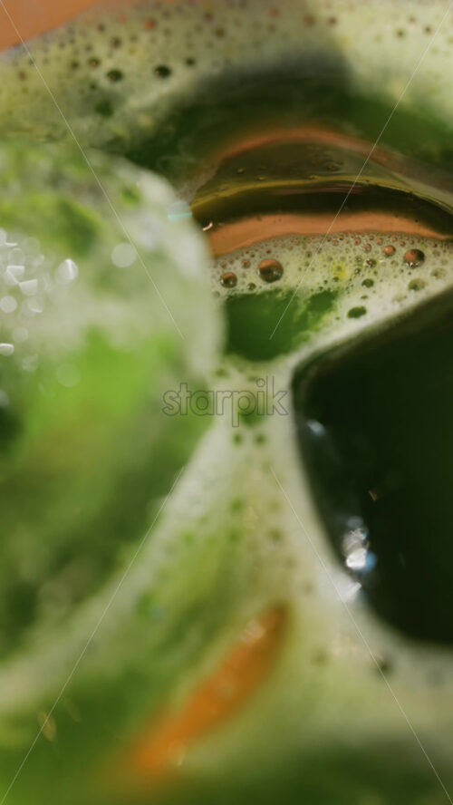 Close up of a glass of an iced orange juice matcha on a table at a cafe. Vertical - Starpik Stock