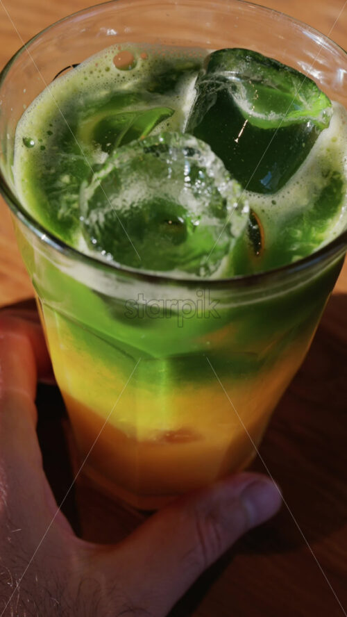 Close up of a glass of an iced orange juice matcha on a table at a cafe. Vertical - Starpik Stock