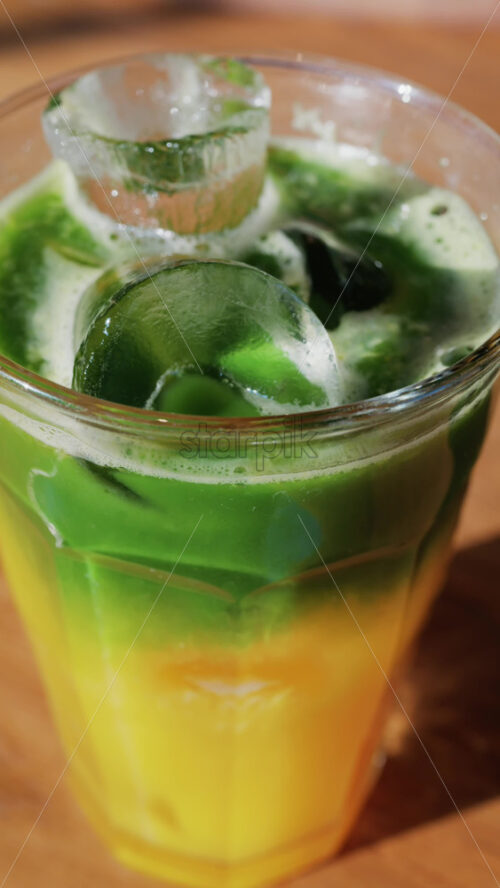 Close up of a glass of an iced orange juice matcha on a table at a cafe. Vertical - Starpik Stock