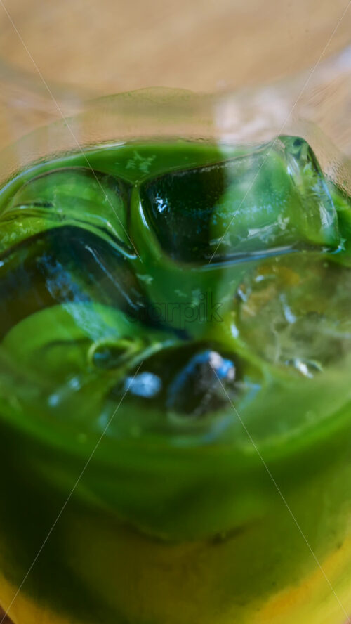 Close up of a glass of an iced orange juice matcha on a table at a cafe. Vertical - Starpik Stock