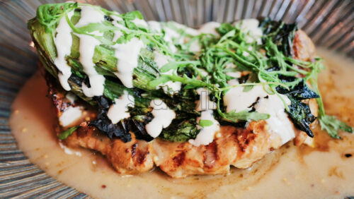 Close up of a grilled chicken breast with charred greens and a creamy dressing on a plate - Starpik Stock