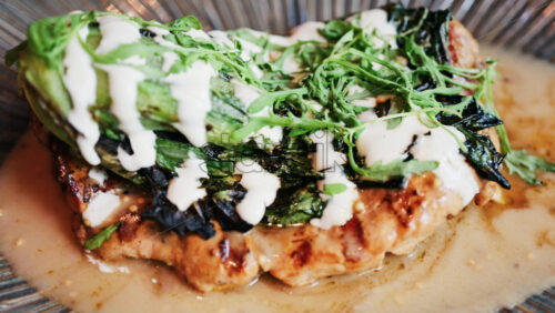 Close up of a grilled chicken breast with charred greens and a creamy dressing on a plate - Starpik Stock