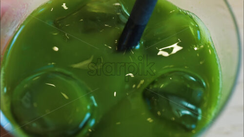 Close up of a hand mixing an iced matcha in a glass with a black straw at a cafe - Starpik Stock
