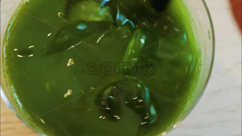 Close up of a hand mixing an iced matcha in a glass with a black straw at a cafe - Starpik Stock