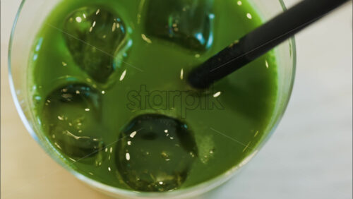 Close up of a hand mixing an iced matcha in a glass with a black straw at a cafe - Starpik Stock