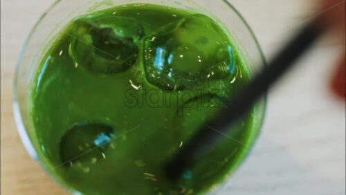 Close up of a hand mixing an iced matcha in a glass with a black straw at a cafe - Starpik Stock