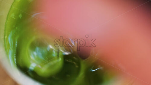 Close up of a hand mixing in a glass of an iced orange juice matcha with a black straw on a table at a cafe - Starpik Stock