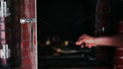 Close up of a hand opening the metal door of a rustic wood-fired oven - Starpik Stock