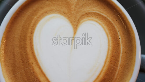 Close up of a heart made on a latte in a black cup - Starpik Stock