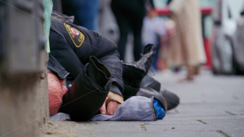 Close-up of a homeless old man sleeping on the pavement wrapped in a black jacket with blurred street on the background in London, England - Starpik Stock