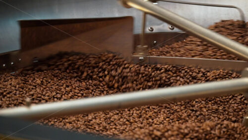 Close up of a large batch of roasted coffee beans being stirred inside a coffee roasting machine - Starpik Stock
