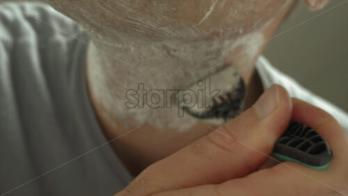 Close up of a man shaving his beard with a green and black razor - Starpik Stock