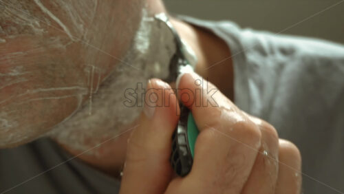 Close up of a man shaving his beard with a green and black razor - Starpik Stock