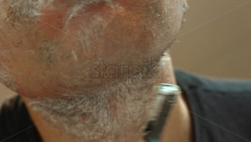 Close up of a man shaving his beard with a green and black razor - Starpik Stock