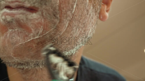 Close up of a man shaving his beard with a green and black razor - Starpik Stock