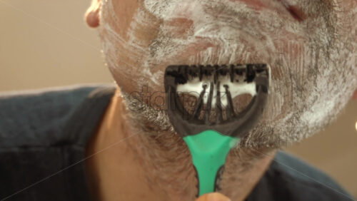 Close up of a man shaving his beard with a green and black razor - Starpik Stock