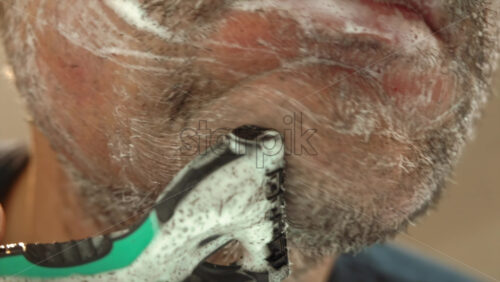 Close up of a man shaving his beard with a green and black razor - Starpik Stock