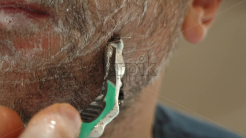 Close up of a man shaving his beard with a green and black razor - Starpik Stock