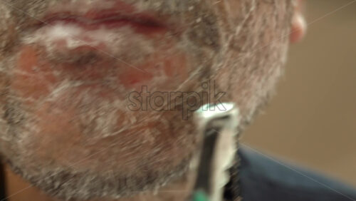 Close up of a man shaving his beard with a green and black razor - Starpik Stock