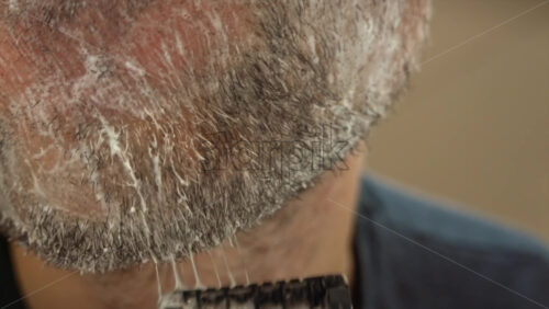 Close up of a man shaving his beard with a green and black razor - Starpik Stock