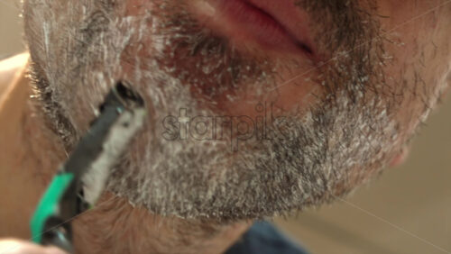 Close up of a man shaving his beard with a green and black razor - Starpik Stock