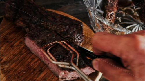Close-up of a man’s hand carving a grilled steak on a rustic wooden cutting board - Starpik Stock