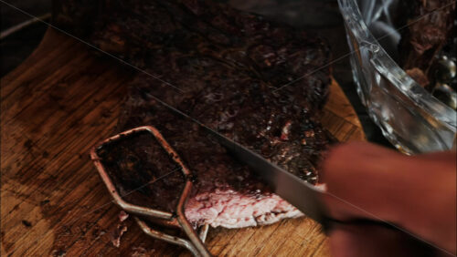 Close-up of a man’s hand carving a grilled steak on a rustic wooden cutting board - Starpik Stock