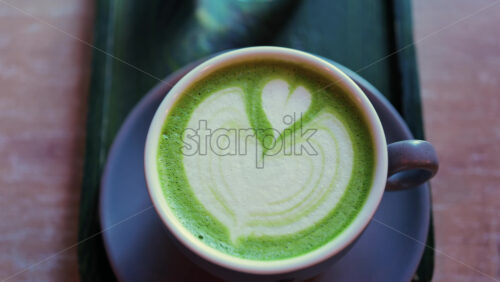 Close up of a matcha latte and a glass of water on a little green tray on a table at a cafe - Starpik Stock