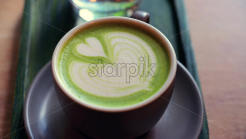 Close up of a matcha latte and a glass of water on a little green tray on a table at a cafe - Starpik Stock