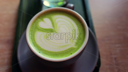 Close up of a matcha latte and a glass of water on a little green tray on a table at a cafe - Starpik Stock