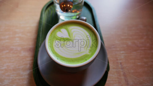 Close up of a matcha latte and a glass of water on a little green tray on a table at a cafe - Starpik Stock