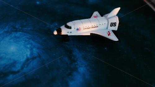Close up of a miniature toy space shuttle placed on a blue cosmic galaxy backdrop - Starpik Stock
