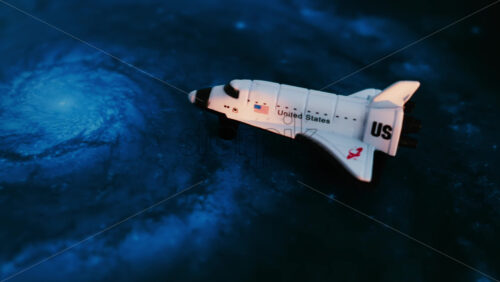 Close up of a miniature toy space shuttle placed on a blue cosmic galaxy backdrop - Starpik Stock